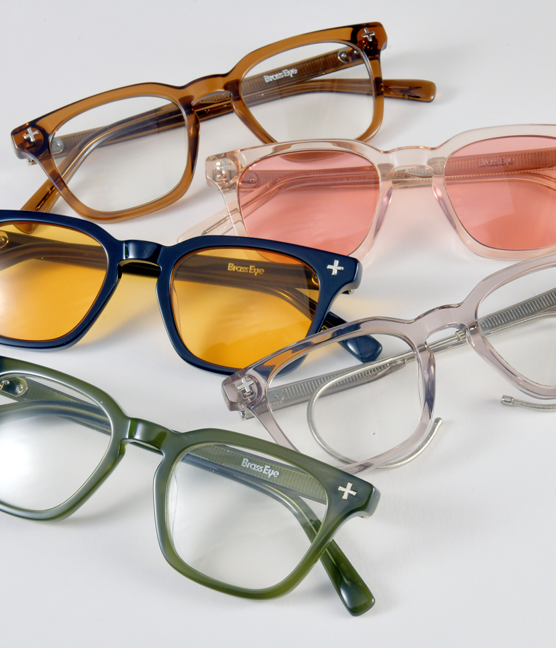 Five pairs of Brass Eye quality safety glasses arranged on a clean white background, each with a different translucent frame color and tinted lens color.